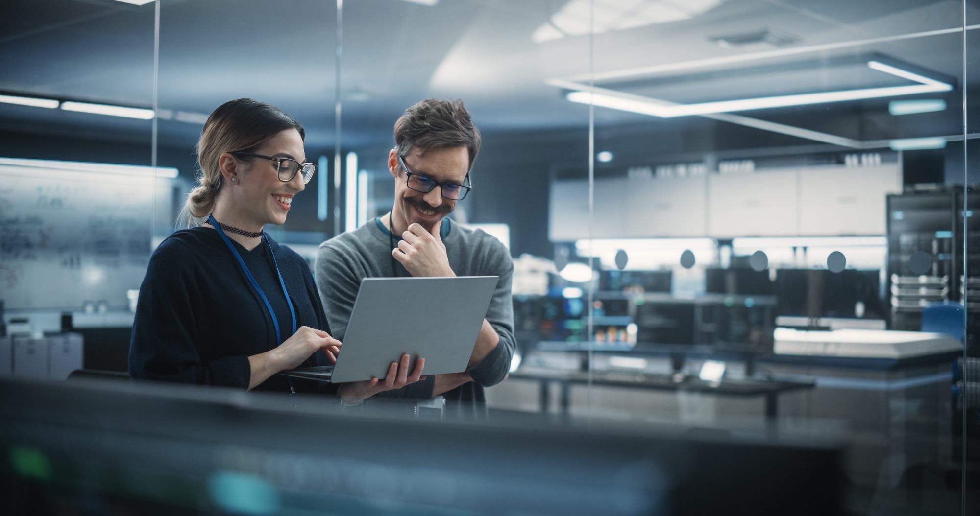 Portrait of Two Creative Young Female and Male Engineers Using Laptop Computer to Analyze and Discuss How to Proceed With the Artificial Intelligence Software. Standing in High Tech Research Office.