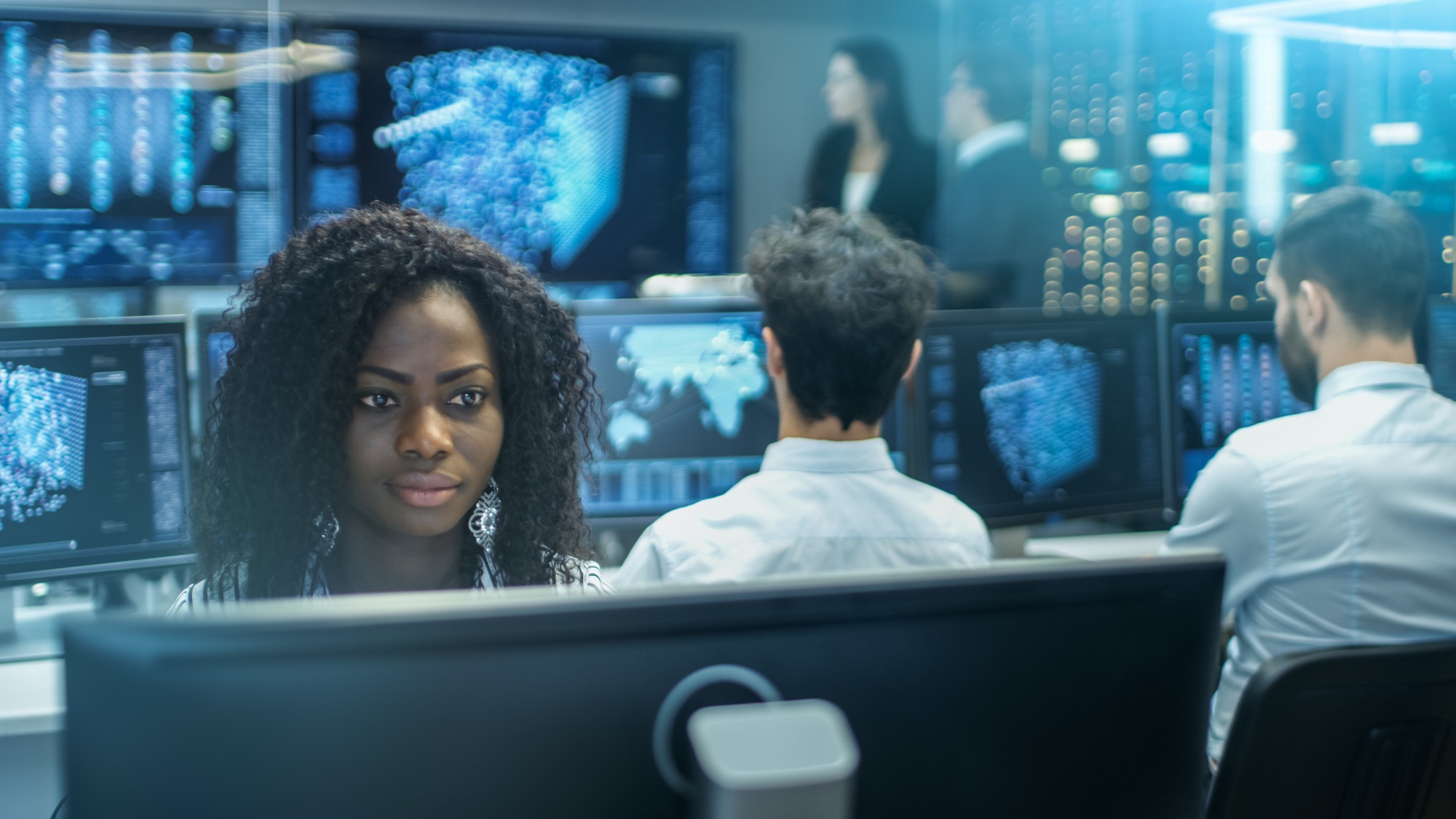 Female Computer Engineer Works on a Neural Network/ Artificial Intelligence Project With Her Multi-Ethnic Team of Specialist. Office Has Multiple Screens Showing 3D Visualization.